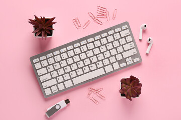 Grey computer keyboard, earphones and flash drive on pink background. Top view