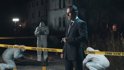 Detective inspecting area and smoking at crime scene at night as forensic experts collect evidence...