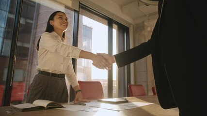 Asian businesswoman shakes hand with man partner in office