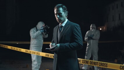 Detective inspecting area and taking notes in notebook at crime scene at night as forensic experts collect evidence behind police tape next to headless body