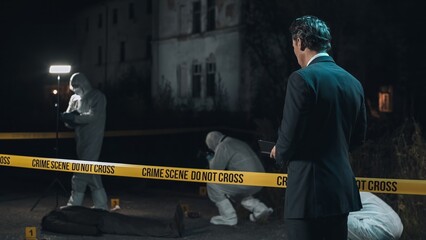 Detective inspecting area and taking notes in notebook at crime scene at night as forensic experts...