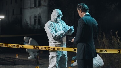 Detective inspecting area and taking notes in notebook at crime scene at night as forensic experts...