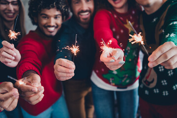 Cropped photo of cheerful young people colleagues hold bengal light cozy christmas party decor spacious office indoors