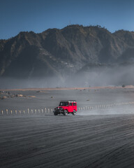 Wide shot of a red 4x4 in volcanic sand.
