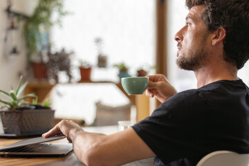 Happy young man in his moment of relaxation turns off the laptop holding a cup of hot milk coffee with his hands, latte art, in his favorite cafe, he enjoys the aroma of coffee and it gives him energy