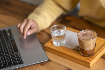 Close-up happy young businesswoman self-employed woman enjoying a caramel coffee and brouni in a specialized coffee shop, works with her laptop, digital nomad, enjoys a coffee on a wooden table