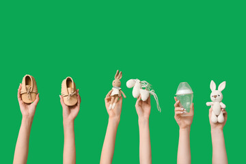 Female hands with knitted toys, baby booties and bottle on green background