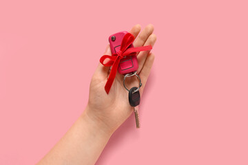 Female hand and gift keys of new car with red bow on pink background, closeup