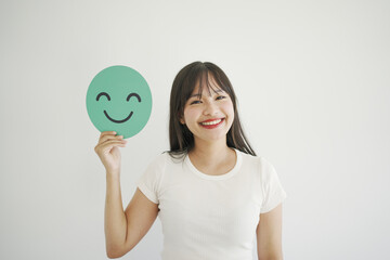 Happy young Asian woman holding smile emoji face, positive mental health, world mental health day concept
