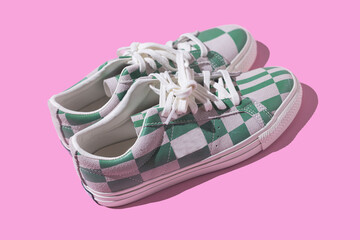 Modern white leather sneakers with green checkered and lined patterns with hard shadow on pink background. Fashionable, modern, eye-catching, quirky and fun concept.