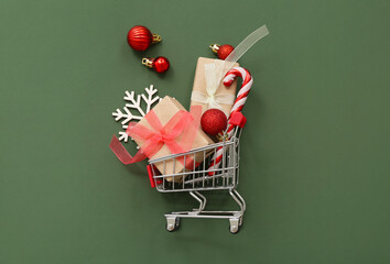 Composition with mini shopping cart, Christmas gifts and decorations on green background