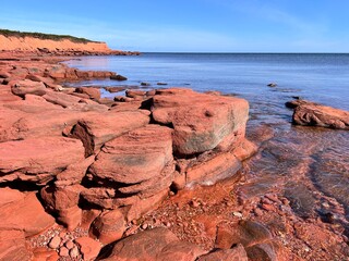 Beautiful red rocks, sculpted by wind and waves, line the shoreline of a pristine, deserted beach...