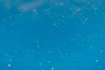 Silver glitter floats in blue water creating a cosmic background