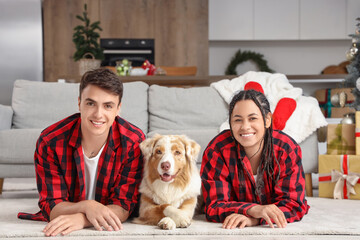 Happy young couple in pajamas with dog lying at home on Christmas eve