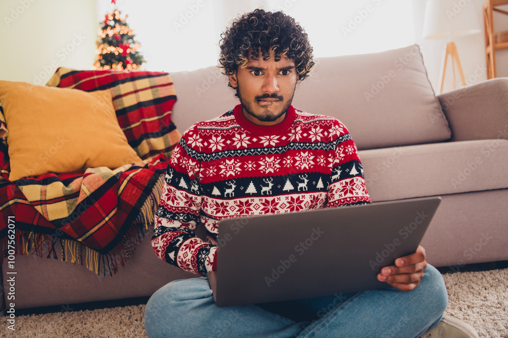 Wall mural Portrait of nice young man use laptop bite lip shop order wear xmas sweater holiday atmosphere flat indoors