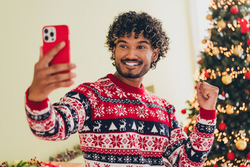Photo of nice young man phone selfie raise fist illumination wear christmas pullover festive time apartment indoors