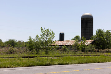 Tallulah, Louisiana, USA - April 23, 2024: Afternoon sun shines on a historic barn and silos of an overgrown farm.