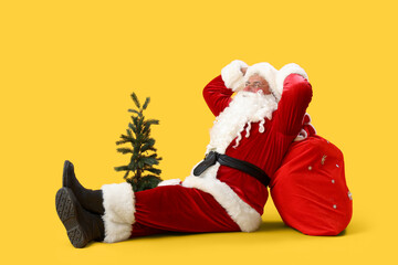 Santa Claus with bag and Christmas tree sitting on yellow background