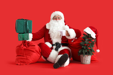Santa Claus with bags, Christmas tree pointing at gift boxes on red background