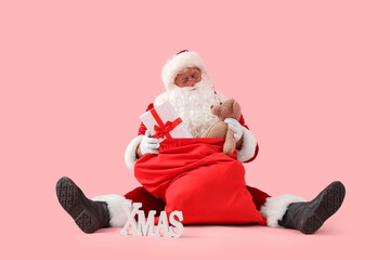 Santa Claus with bag, Christmas gifts and word XMAS sitting on pink background
