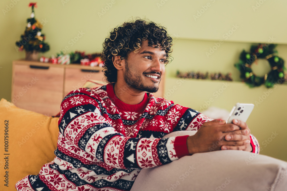 Wall mural Portrait of nice young man sit couch hold phone fantasize wear xmas sweater holiday atmosphere flat indoors