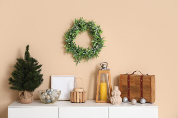 Chest of drawers with Christmas decorations and wreath on wall in room