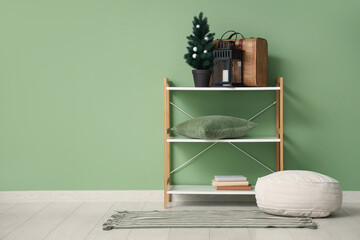 Shelving unit with  Christmas tree, suitcase, lantern and pouf near green wall