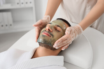 Beautician applying cosmetic gel mask on handsome man's face in spa salon