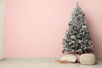 Decorated Christmas tree with rug, cushions and pouf near pink wall