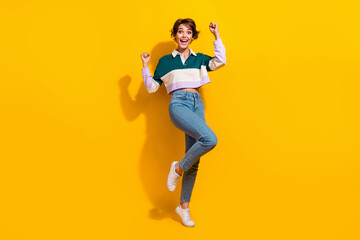 Fototapeta na wymiar Full length photo of pretty lucky woman wear polo shirt rising fists isolated yellow color background