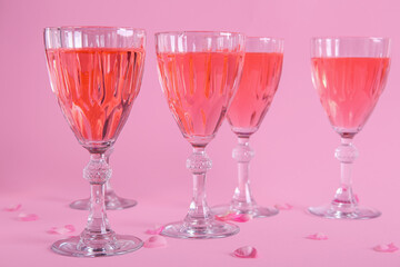 Glasses of tasty pink wine and rose petals on color background