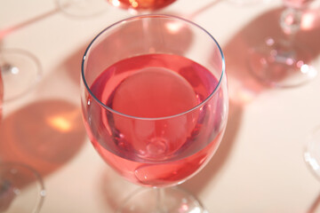Glass of tasty pink wine on beige background, closeup