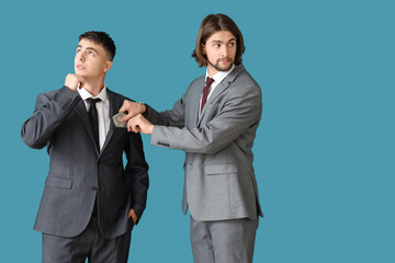 Young businessman putting bribe into man's pocket on blue background. Corruption concept