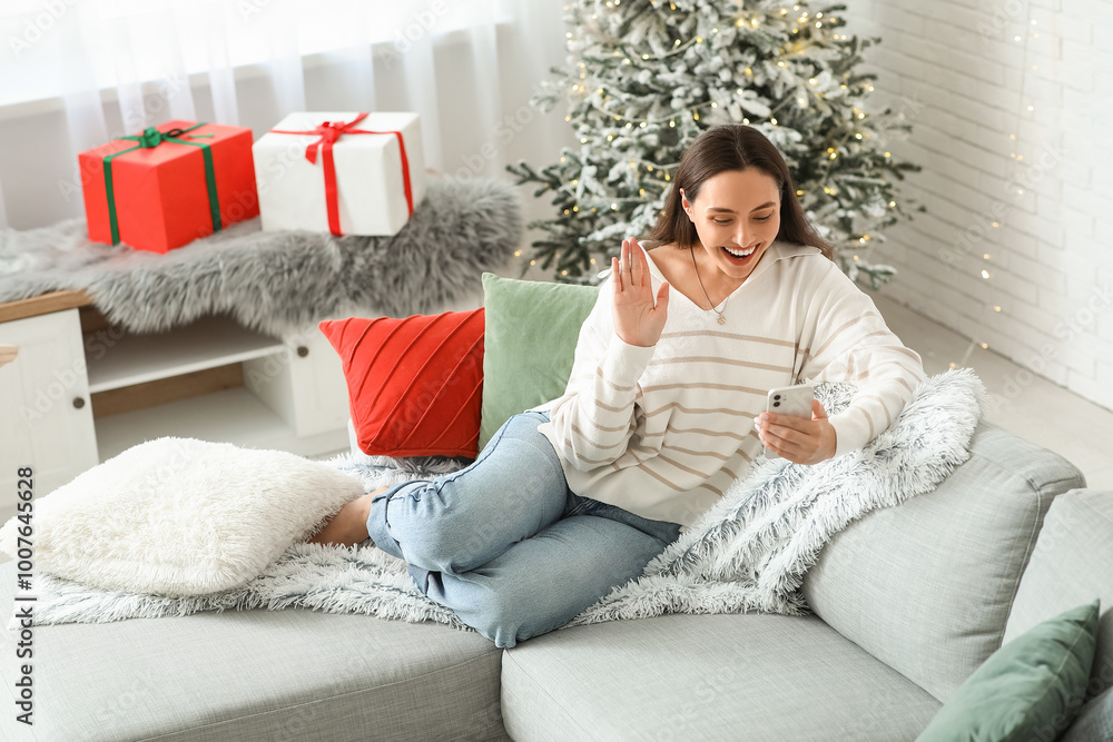 Wall mural Beautiful young woman taking selfie and sitting on sofa in living room. Christmas celebration