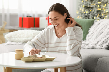 Beautiful young woman writing Christmas letter to Santa in living room