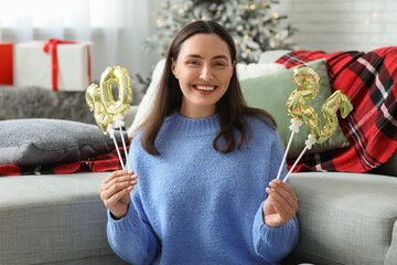 Beautiful young woman with figure 2025 made of foil balloons in living room. Christmas celebration