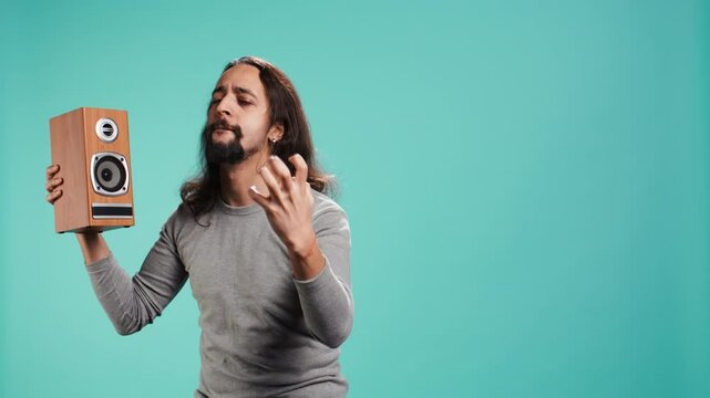 Portrait of person having fun holding speakers, listening music, dancing on rhythm. Cheerful man entertaining himself hearing songs with powerful bass, nodding head, studio background, camera B