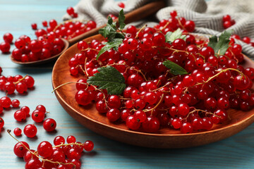Fresh red currants and leaves on light blue wooden table, closeup