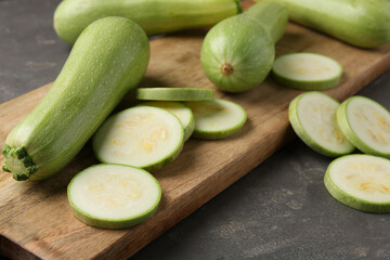 Board with fresh cut and whole zucchinis on grey textured table, closeup