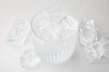 Refreshing water in glass with ice cubes on light background, closeup