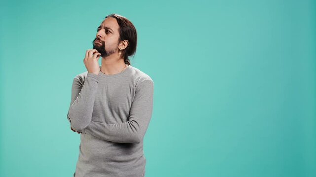 Pensive man deep in thoughts, doing ruminating hand gesturing, isolated over studio background. Unsure person doing stroking chin gesture, thinking, studio backdrop, camera B