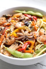 Stir-fry noodles with sea food in bowl on white table, closeup