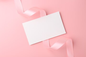 Blank card and ribbon on pink background, top view