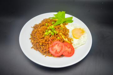 Indonesian fried noodle with sunny side up, tomato slices and lettuce