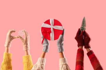 Women in warm gloves with Christmas decor and gift box on pink background