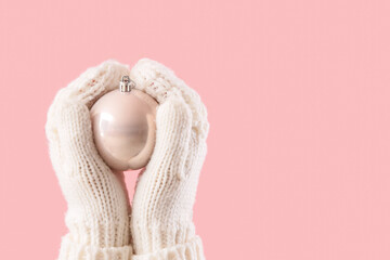 Woman in warm gloves with Christmas ball on pink background, closeup