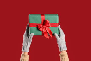 Woman in warm gloves with Christmas gift box on red background