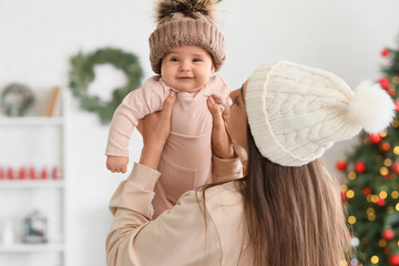 Happy mother with her little baby in warm hats at home on Christmas eve