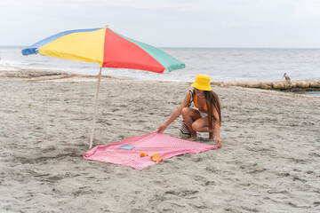 Woman preparing a beach picnic under a colorful umbrella by the ocean