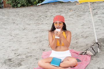 Latin woman using a smartphone while relaxing on the beach